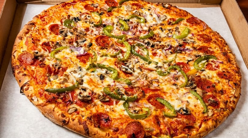 A large, hot pizza with pepperoni, green peppers, mushrooms, and onions in a cardboard box.