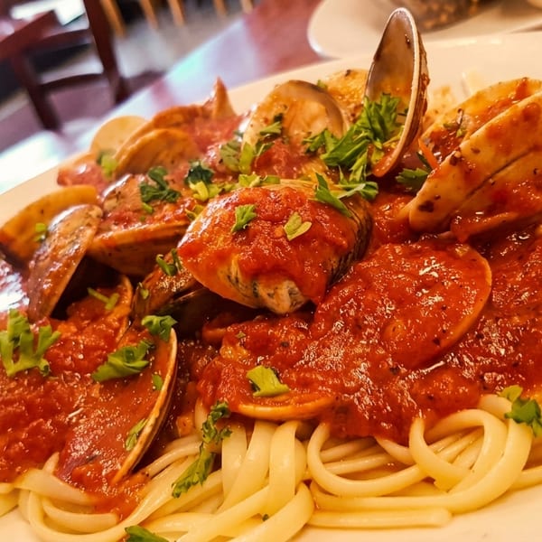Linguine pasta with clams and red sauce, garnished with fresh parsley, on a white plate.