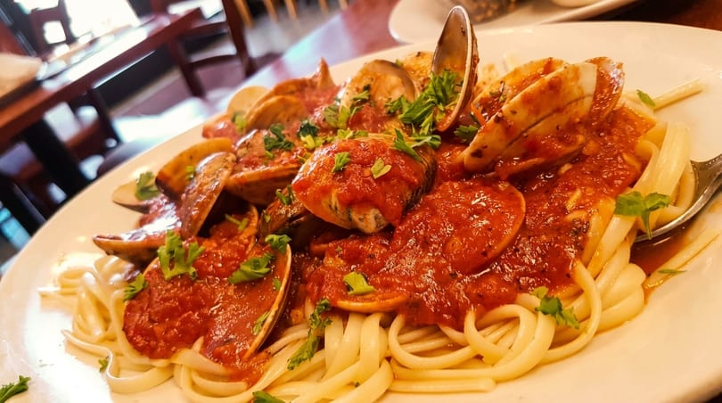 Linguine pasta with clams and red sauce, garnished with fresh parsley, on a white plate.