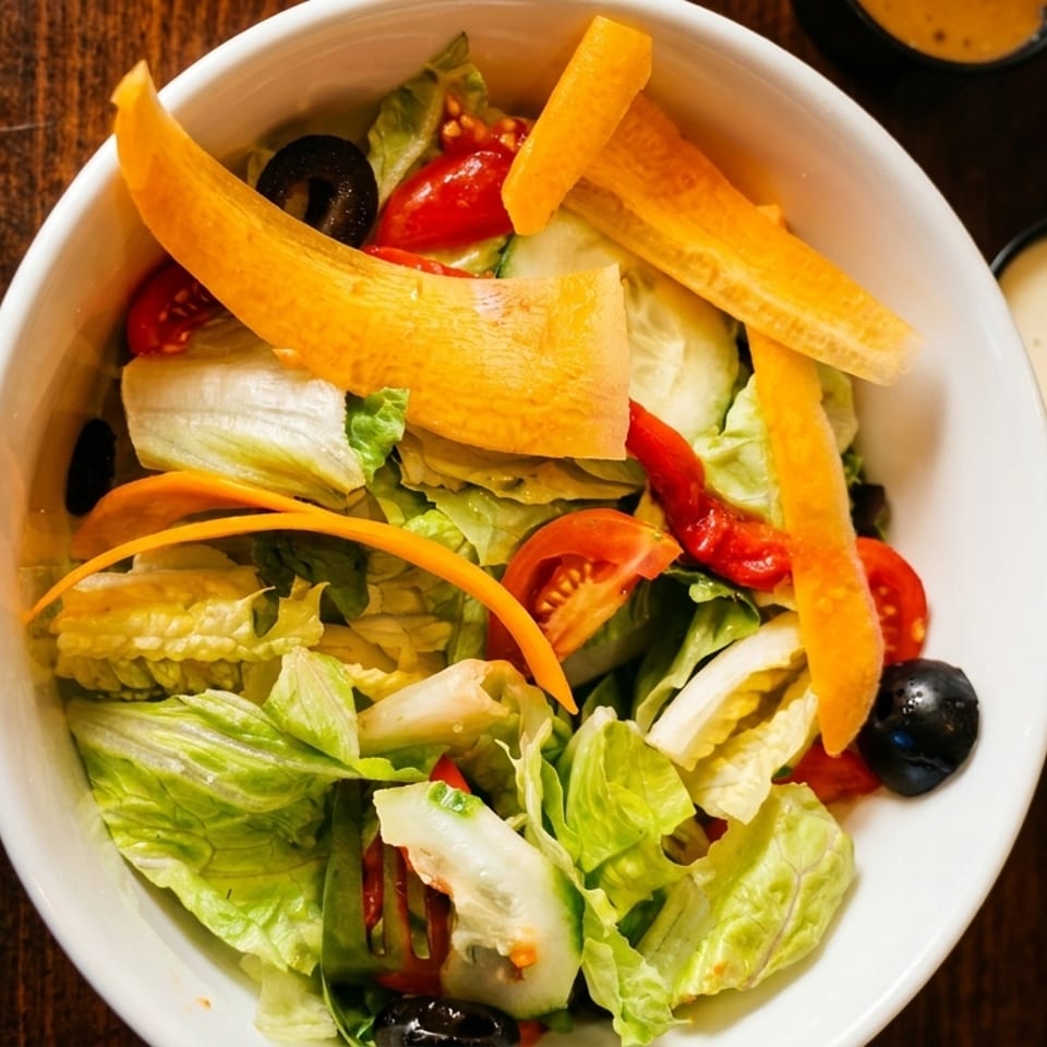 Overhead view of a fresh garden salad with lettuce, tomatoes, olives, and carrot strips in a white bowl.