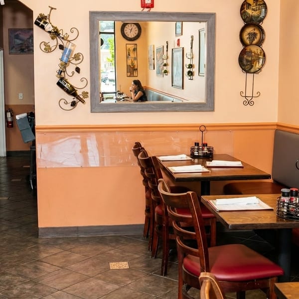 Cozy restaurant interior with booth seating, wooden tables, and a mirror reflecting a diner.