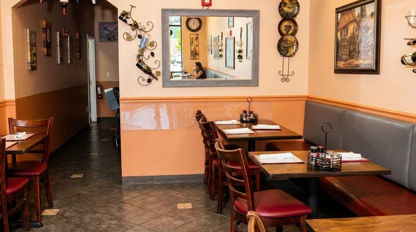 Cozy restaurant interior with booth seating, wooden tables, and a mirror reflecting a diner.