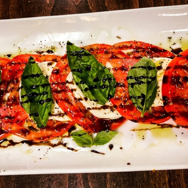 Caprese salad with sliced tomatoes, fresh mozzarella, basil leaves, and balsamic glaze on a white plate.