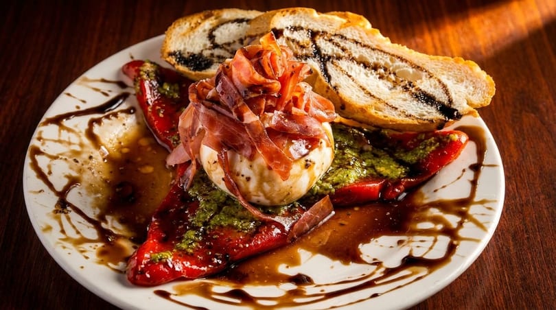 Burrata cheese topped with prosciutto, pesto, roasted red peppers, and balsamic glaze with bread.